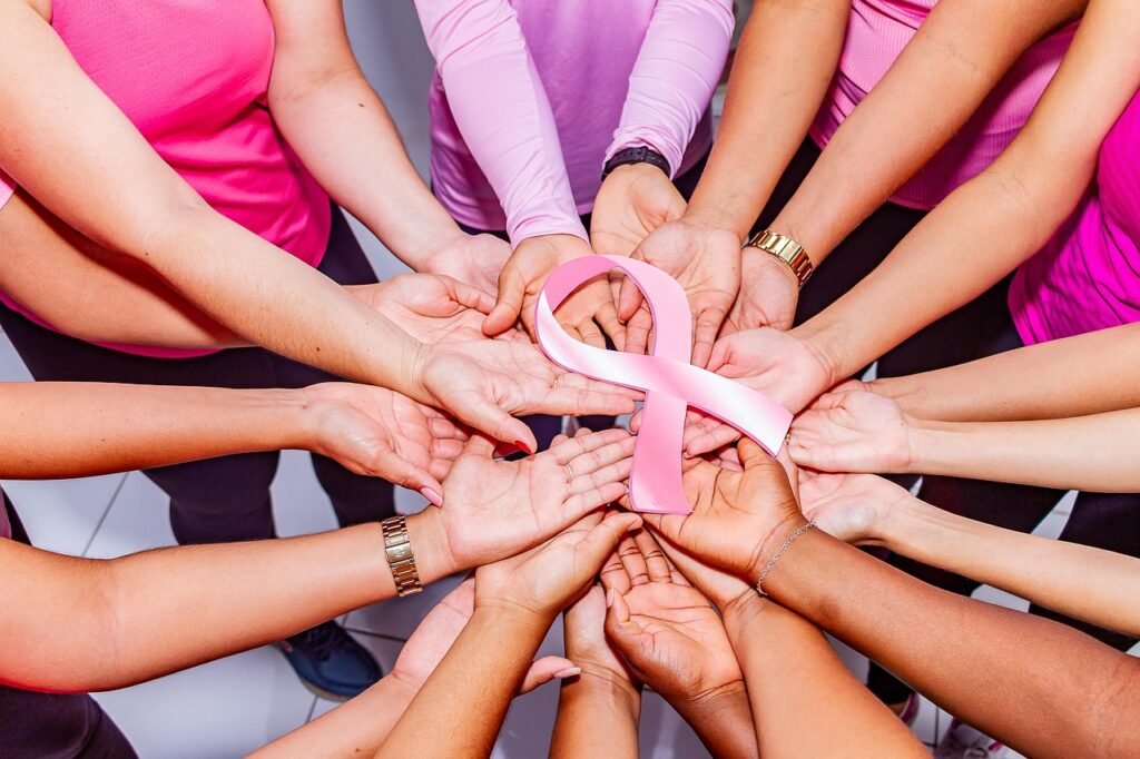 Multiple hands holding a pink breast cancer ribbon